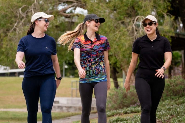 Three happy healthy women walking together outdoors wearing hats and exercise clothing