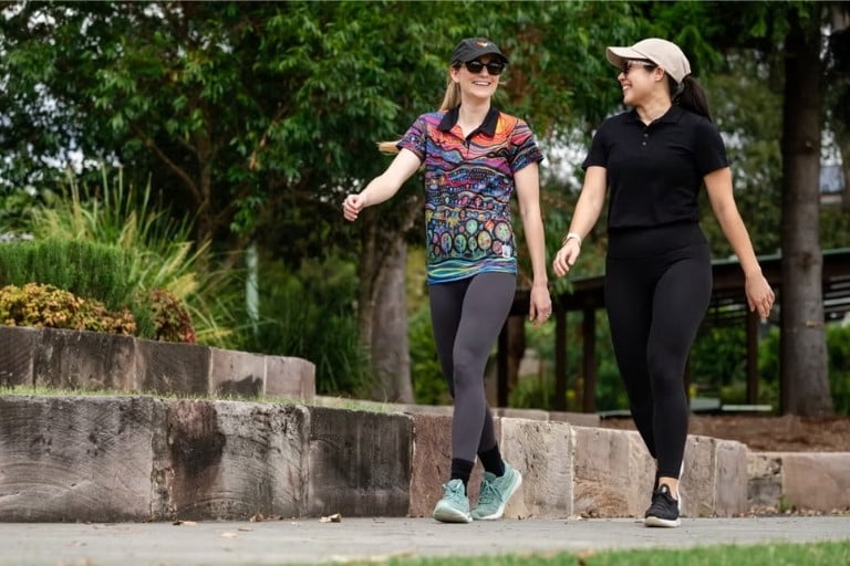 Two happy healthy women walking together outdoors wearing hats and exercise clothing