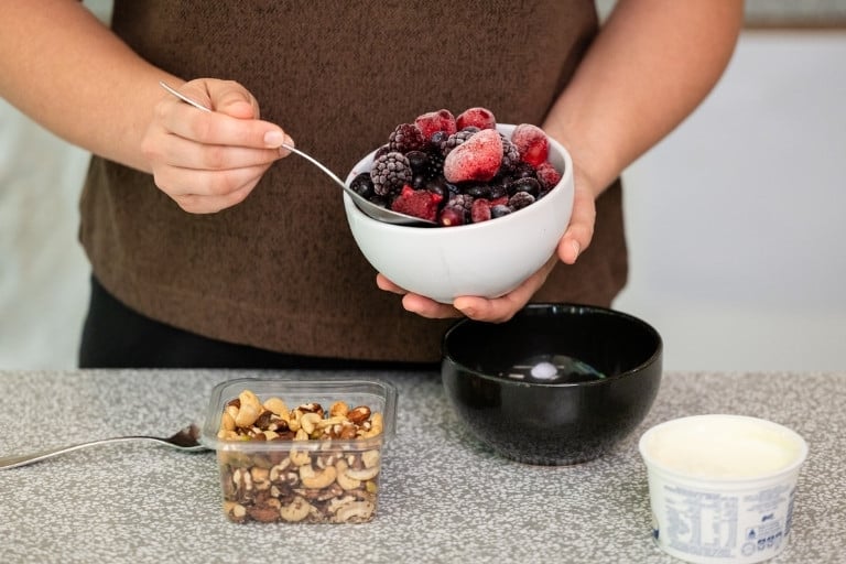 Woman making healthy breakfast in the kitchen using yoghurt, berries and mixed nuts