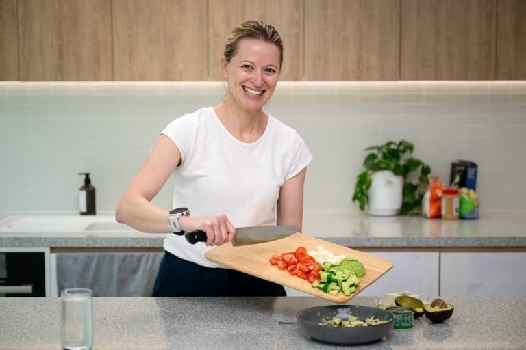 Woman preparing healthy meal in the kitchen, cutting up salad ingredients on a chopping board