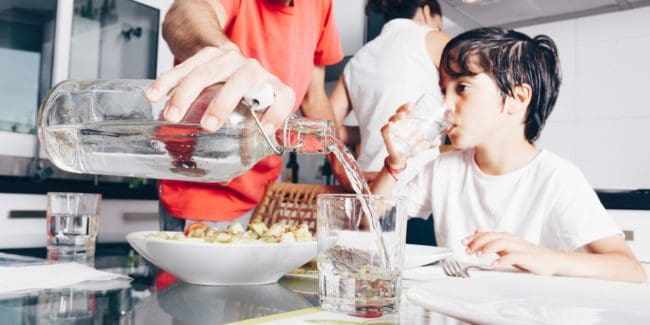 Father pouring a glass of water for his son at the dinner table