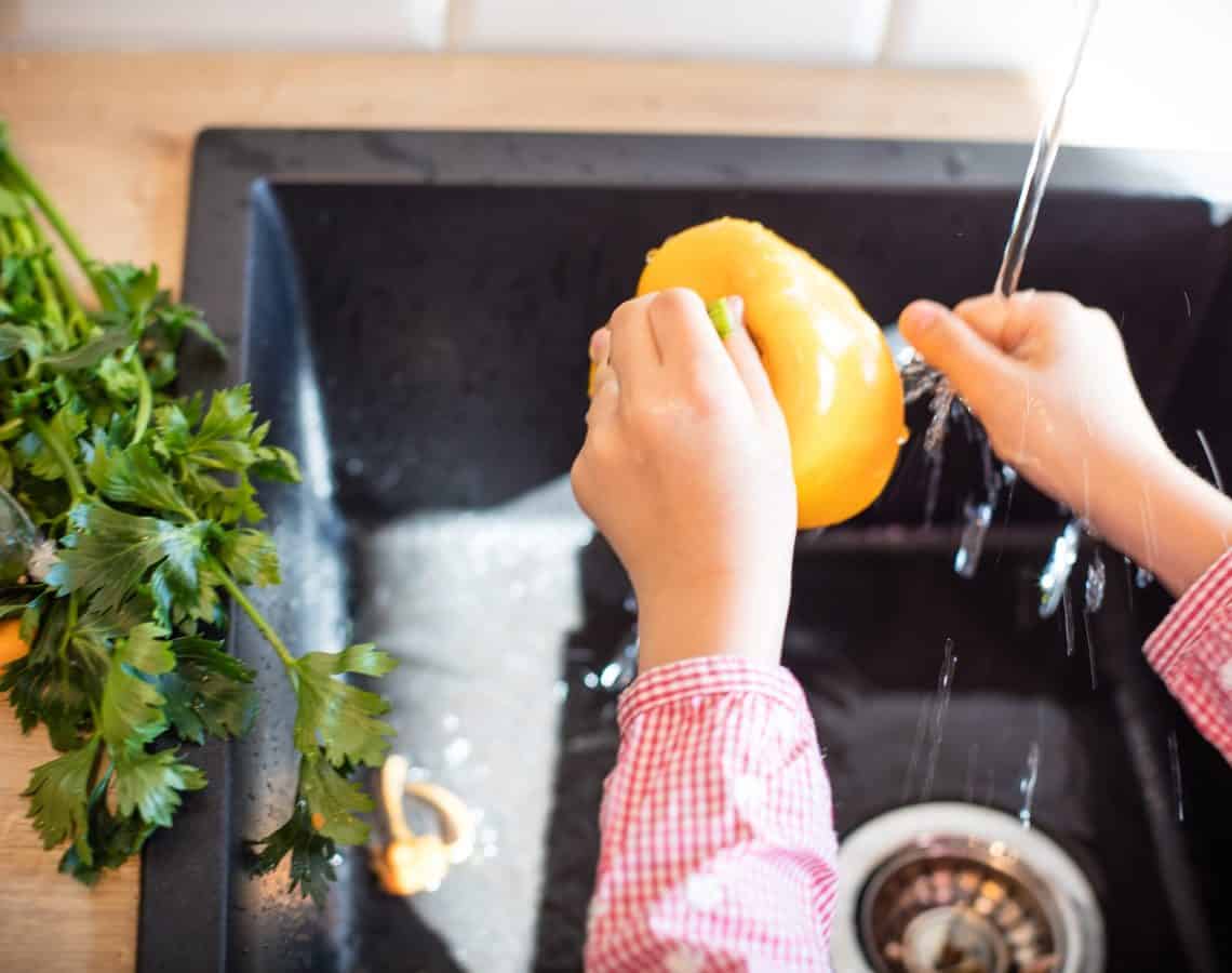 Child washing a yellow capsicum