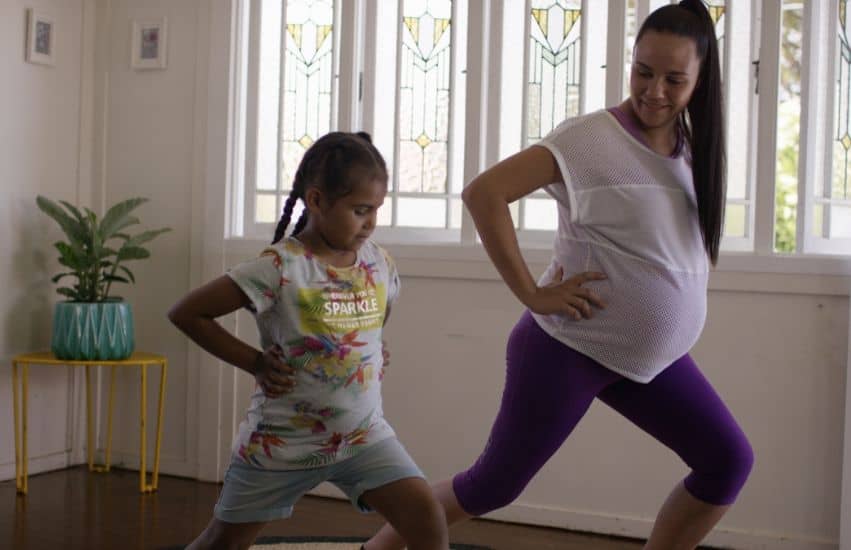 Pregnant woman and her daughter doing light exercise in their house