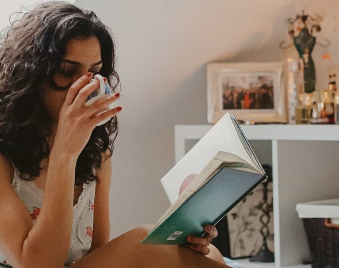 Woman reading and drinking tea in bedroom