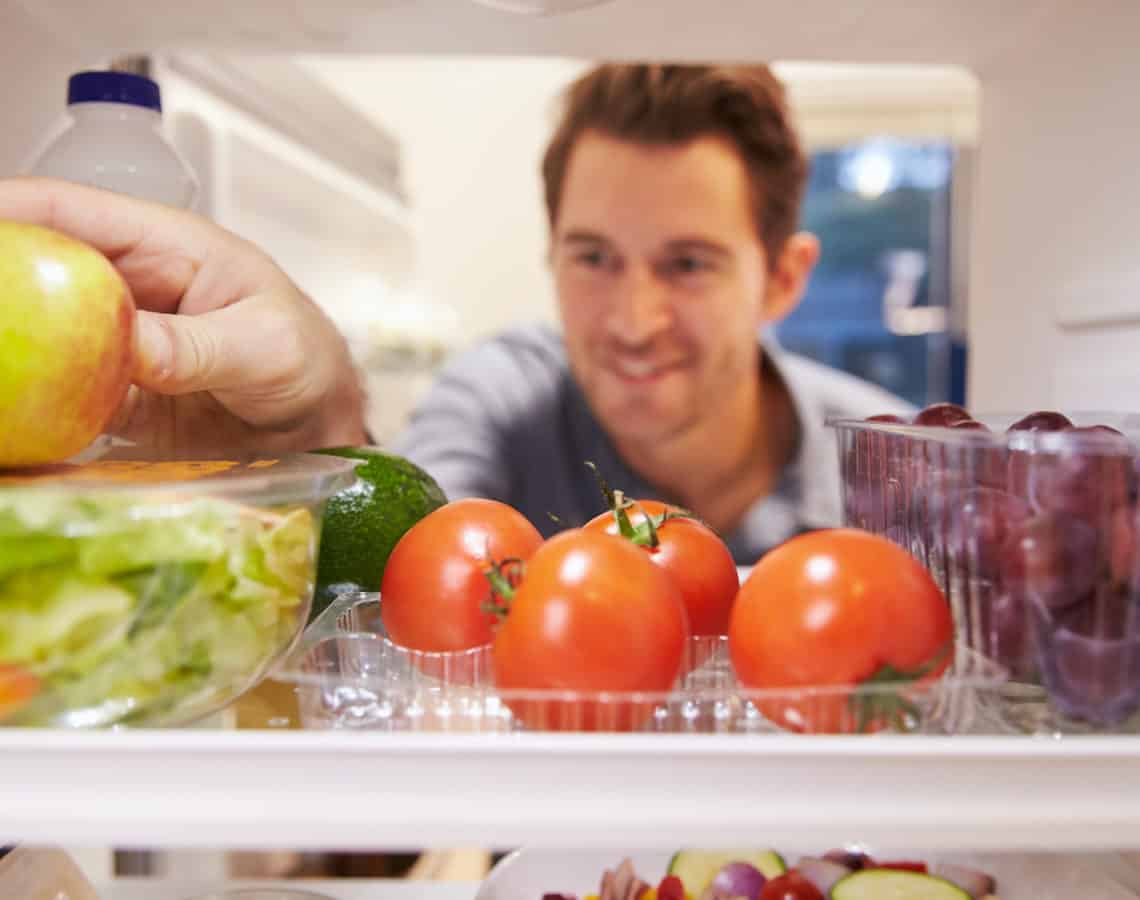 Man reaching inside fridge for a piece of fruit