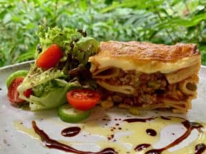 Lasagne and side salad on a plate with a drizzle of olive oil and balsamic vinegar