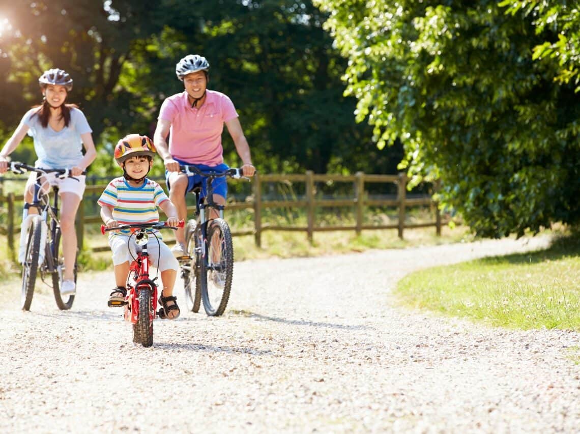 A mum and dad are riding bikes with a young boy on an off road track.