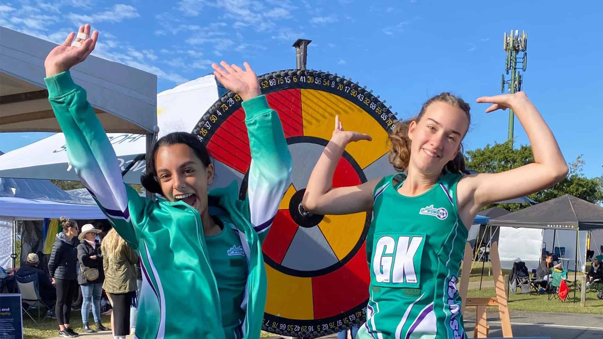 Netballers jump for joy beside the Health and Wellbeing Queensland prize wheel