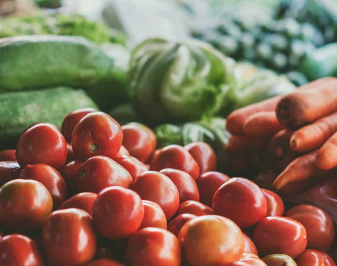 A pile of fresh vegetables including cherry tomatoes, carrots and cucumber