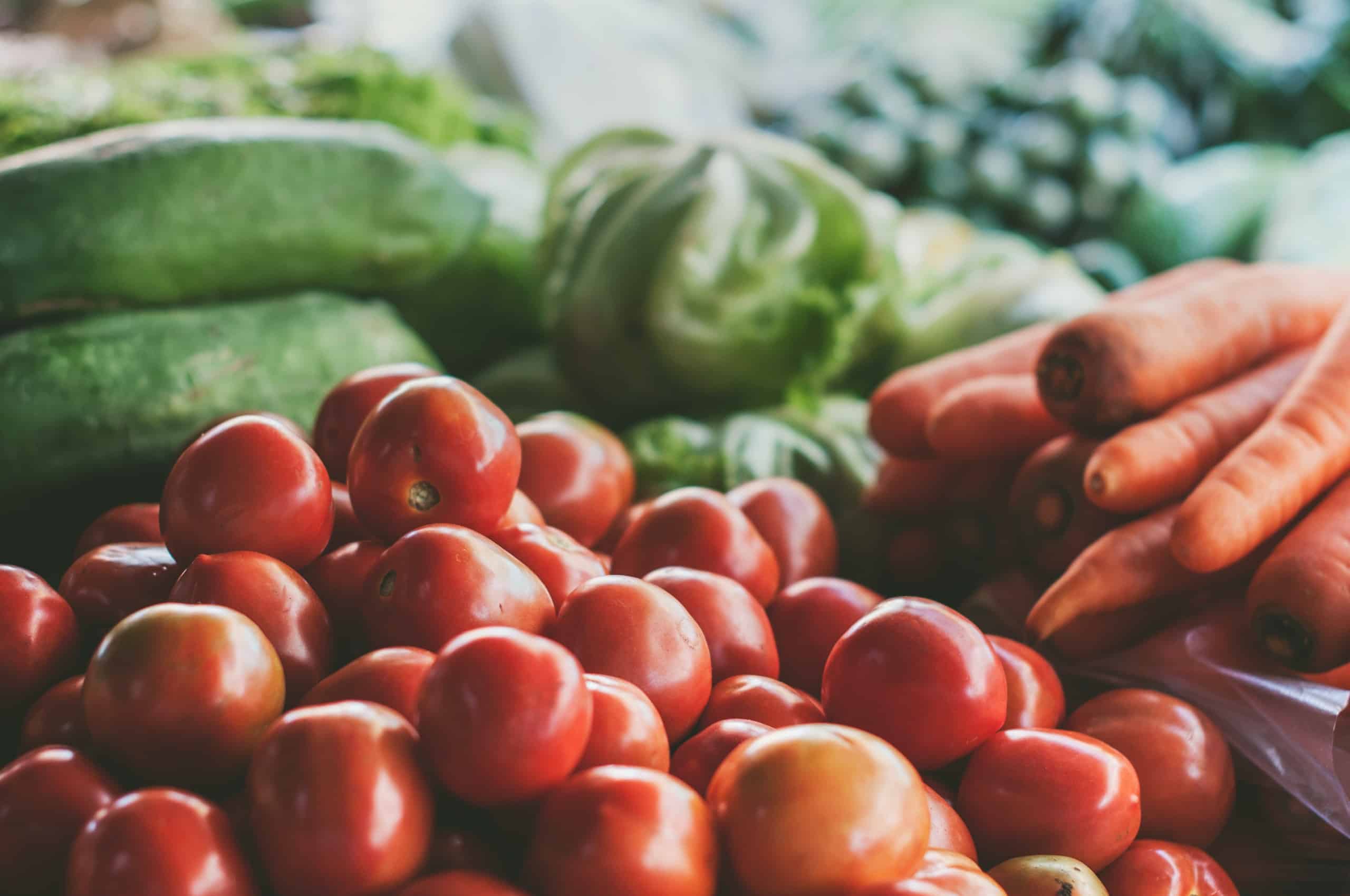A pile of fresh vegetables including cherry tomatoes, carrots and cucumber
