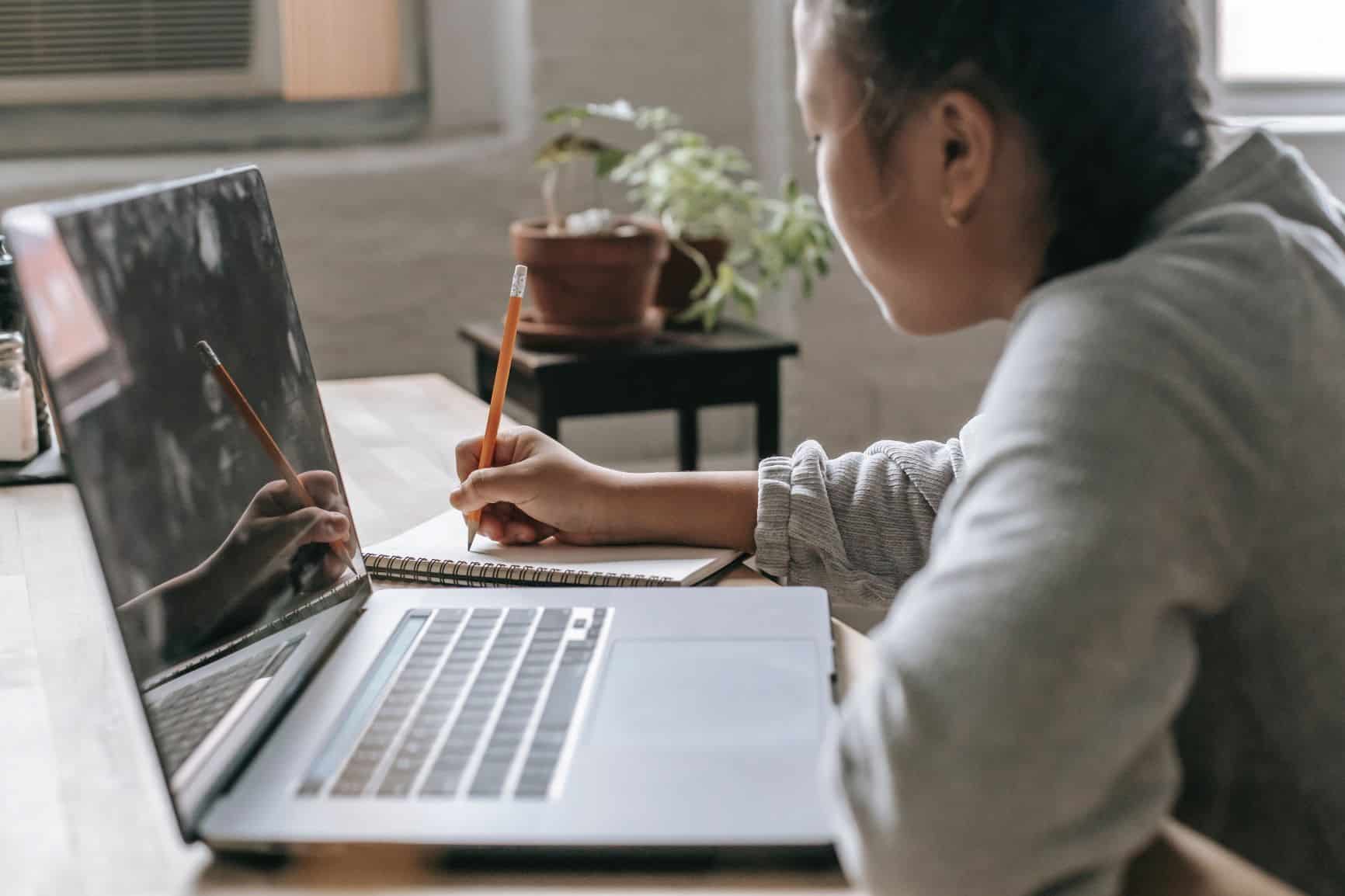 A woman is making notes in a notebook while sitting in front of a laptop