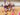 Two Firebirds players sitting on an indoor netball court with four young netball players under 5 years of age.