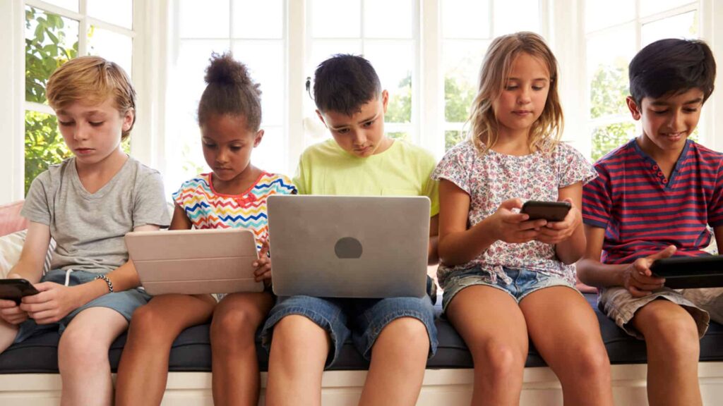 Children sitting with laptops, phones and tablets