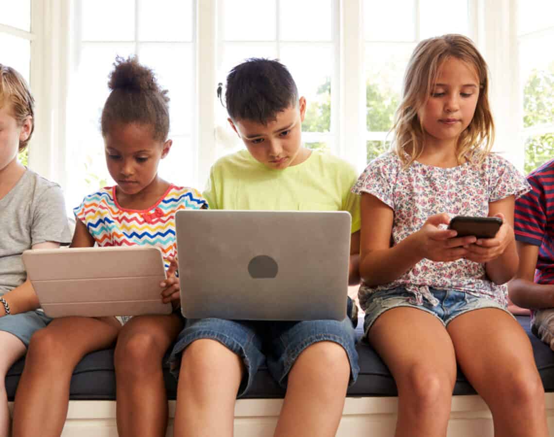 Children sitting with laptops, phones and tablets