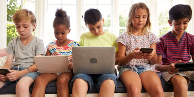 Children sitting with laptops, phones and tablets