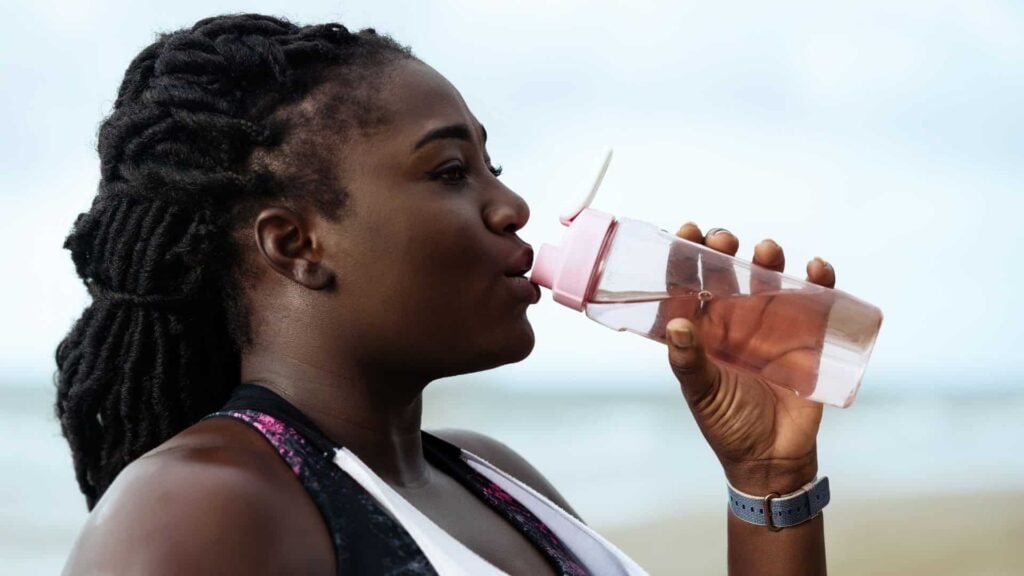A woman drinking water from a pink water bottle.