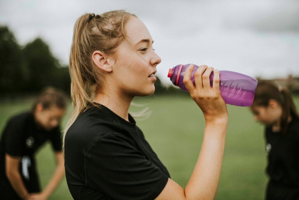women drinks water from a water bottle during a break from an outdoor sports activity