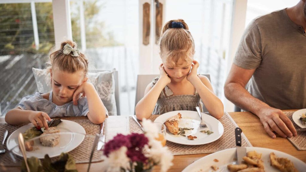 Two young girls sitting at dining table staring at the dinner on their plate