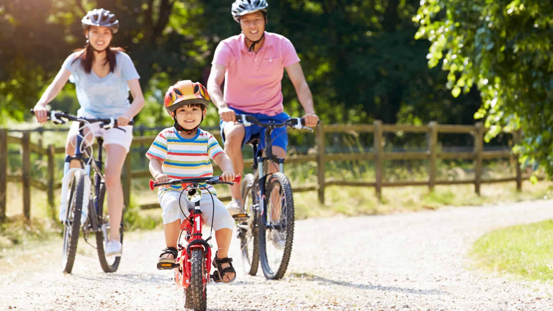 Man, woman and young boy ride their bikes on gravel pathway wearing helmets