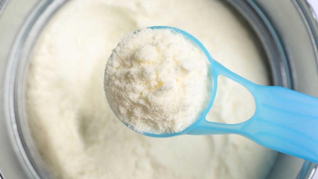 A blue scoop of powdered toddler milk above a tin of toddler milk.