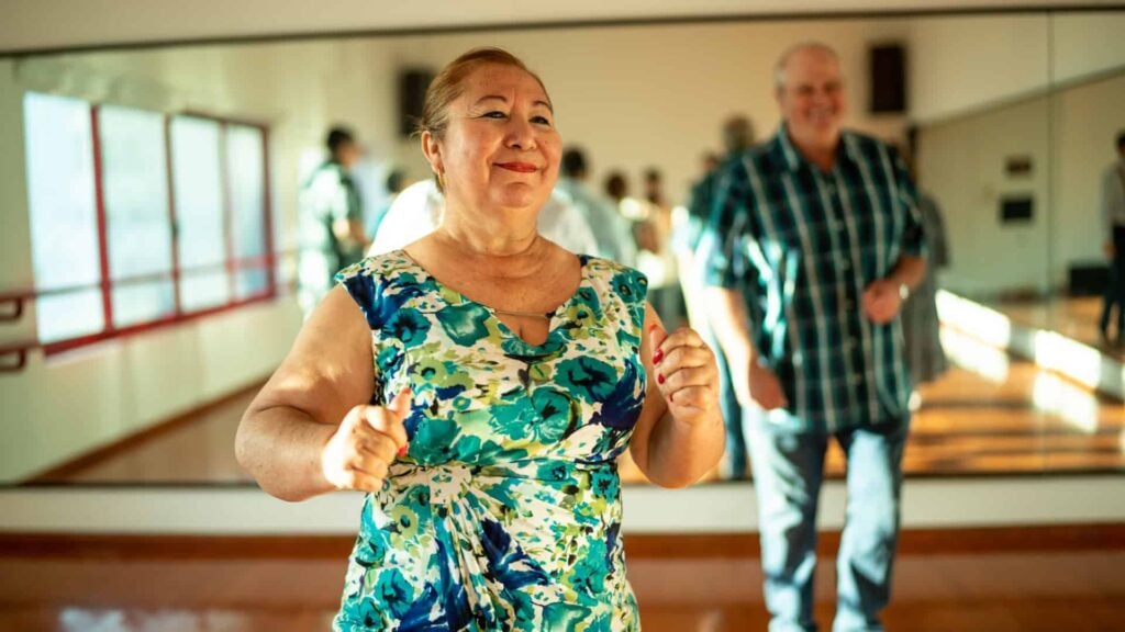 Mature aged women in dance class with older gentleman behind her in background
