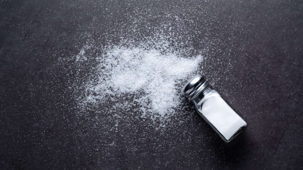 salt shaker and sprinkling of salt across black background