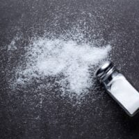 salt shaker and sprinkling of salt across black background