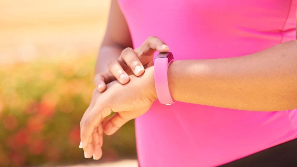 A woman wearing a pink top looking at a step tracker on her left wrist.