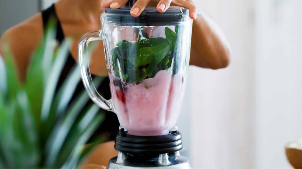 Close up of a blender with pink liquid and fresh spinach leaves