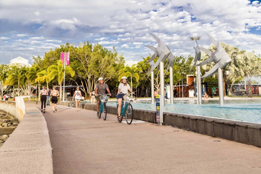 Man and woman ride bikes along an esplanade wearing helmets