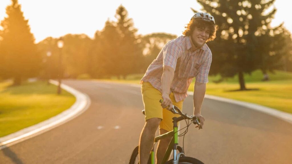 Young man stands up on his bike in the street smiling at camera
