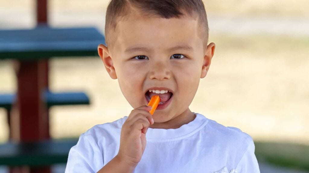 A child taking a bit out of a carrot stick.