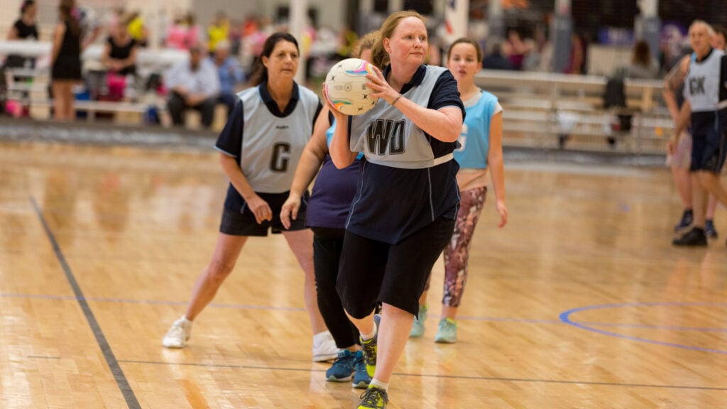 Women playing walking netball on an indoor netball court