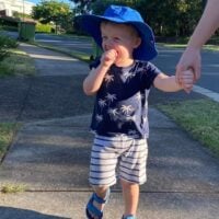Young boy wearing blue hat walks outside holding his mother's hand