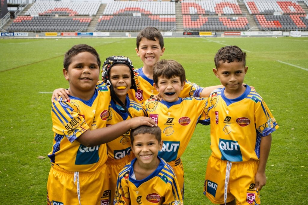 A group of young boys wearing yellow rugby outfits standing on a green rugby field.