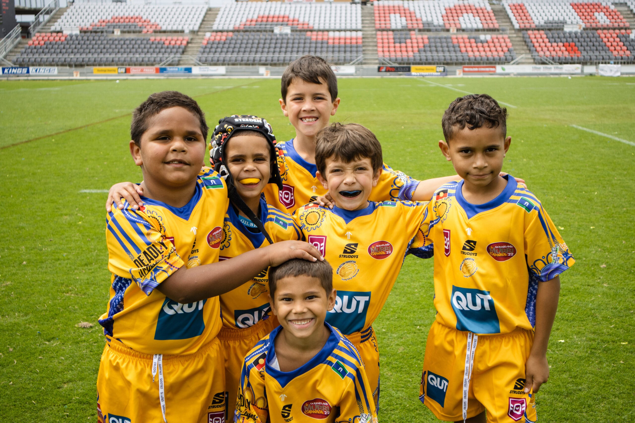 A group of young boys wearing yellow rugby outfits standing on a green rugby field.
