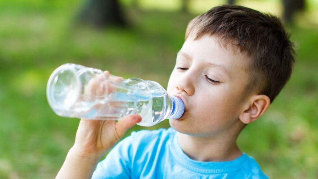 Boy drinks water from a clear water bottle