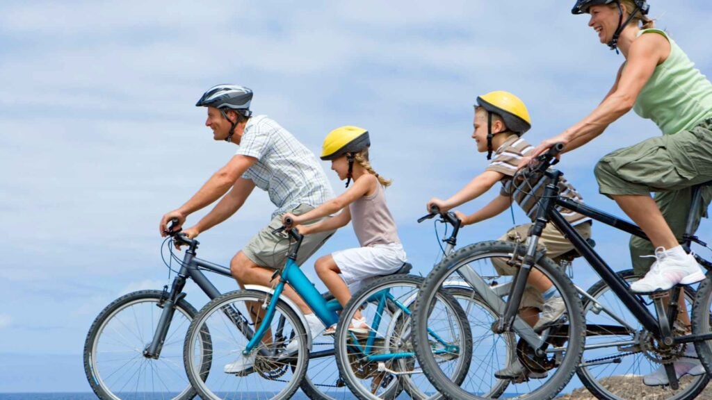 Family of 4 bike riding along the waterfront wearing helmets
