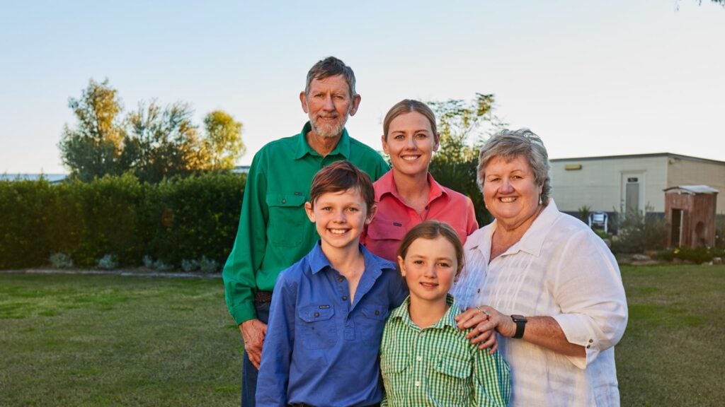 A smiling family with three children standing outside in a rural Queensland backyard.