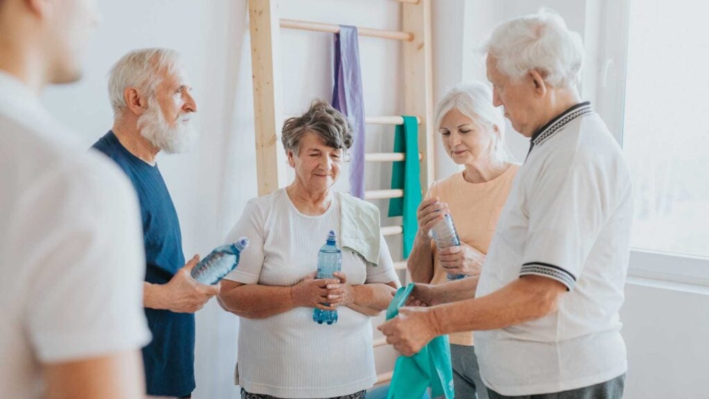 4 older adults stand talking together after a group exercise class