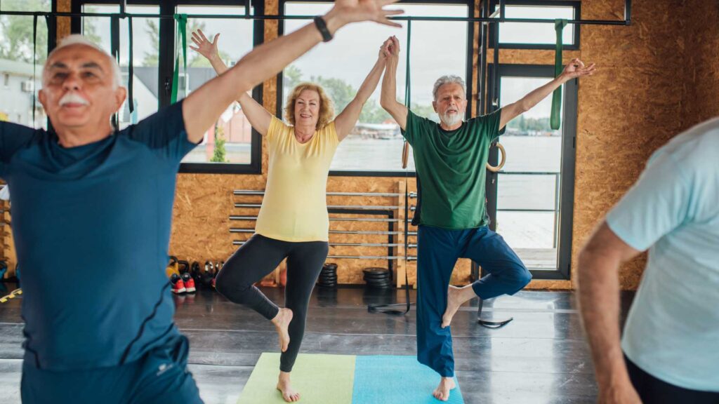 Two older people balance on one leg on their yoga mats
