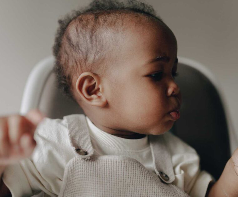 Young boy holding piece of food whilst sitting in highchair