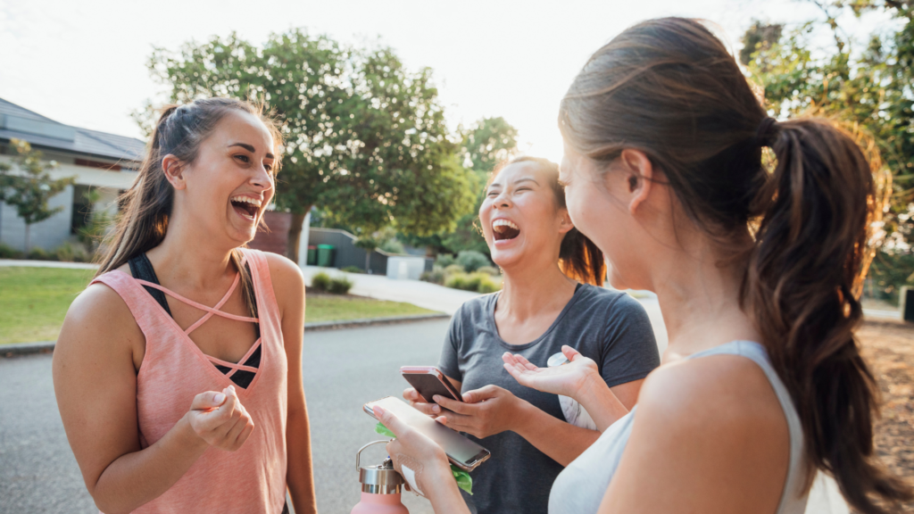 3 young women laugh together on the street engaged in a conversation