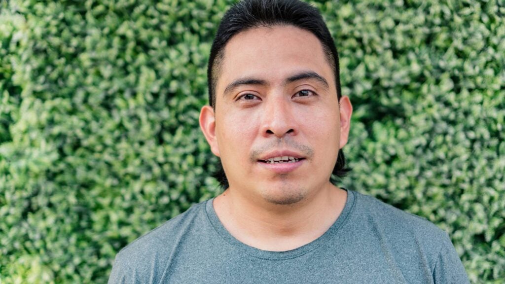 Middle aged man stands in front of a hedge looking directly at the camera