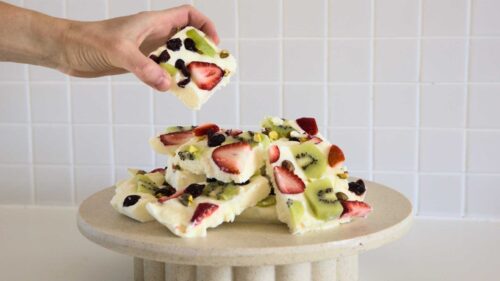 Hand reaches for a slice of yoghurt bark from a pile of them