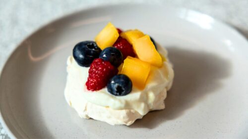Mini meringue nest topped with Greek yoghurt and fresh raspberries, blueberries and mango