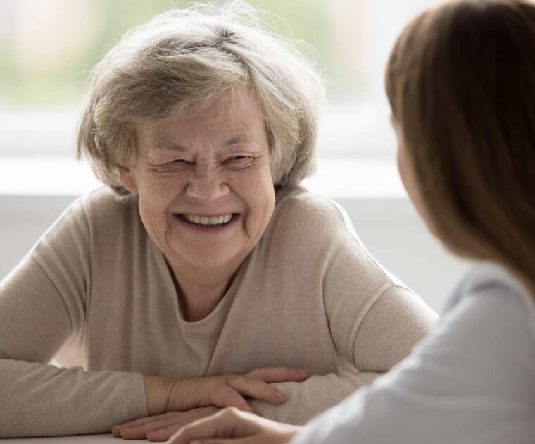 Older lady with beige top smiling at another person.