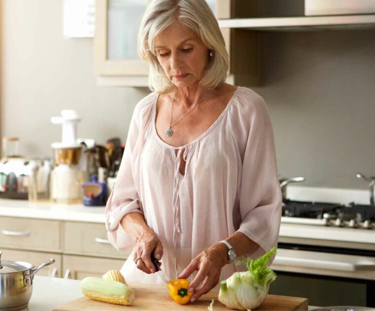 Woman in kitchen cutting vegetables on a chopping board.