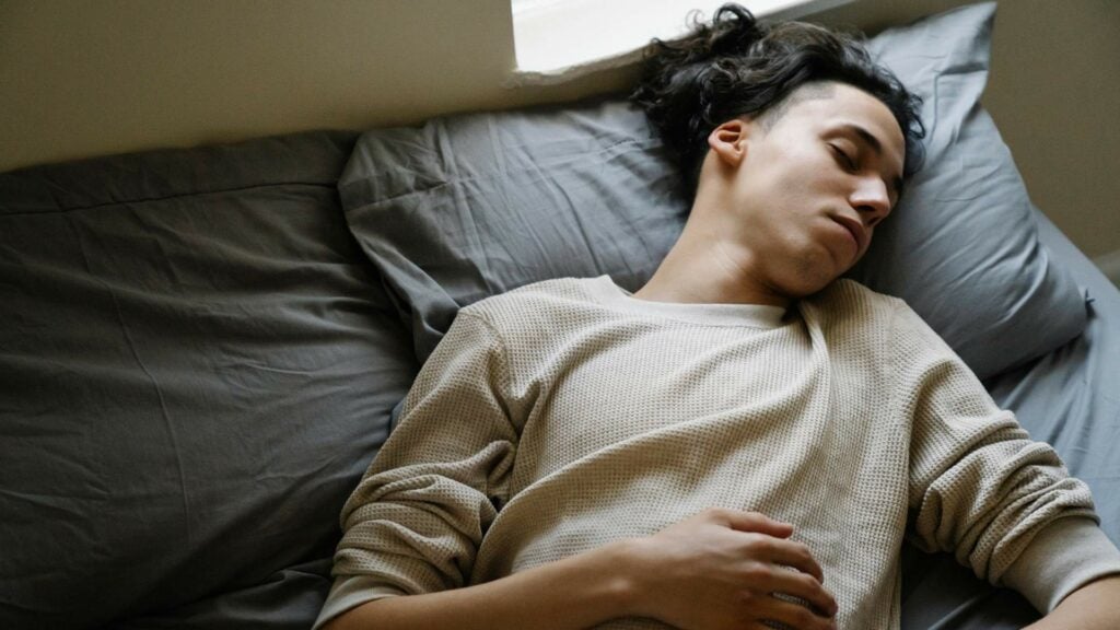 Teenager sleeping on bed with grey bedsheets.