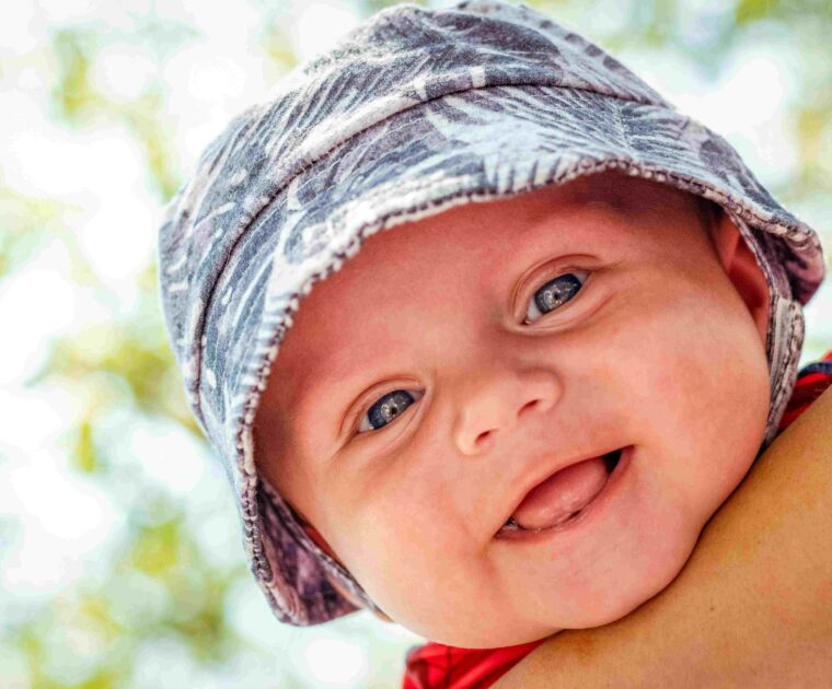Baby boy with hat on outside smiling